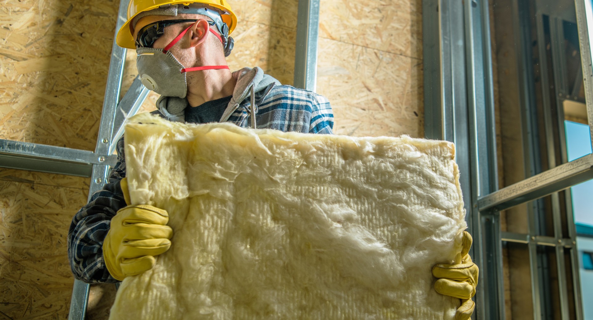 Caucasian Construction Worker Wearing Safety Mask Moving Pieces of Mineral Wool Insulation.